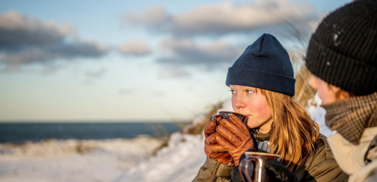 Kvinde holder sig varm med varm drik i klitterne en vinterdag i Klitmøller