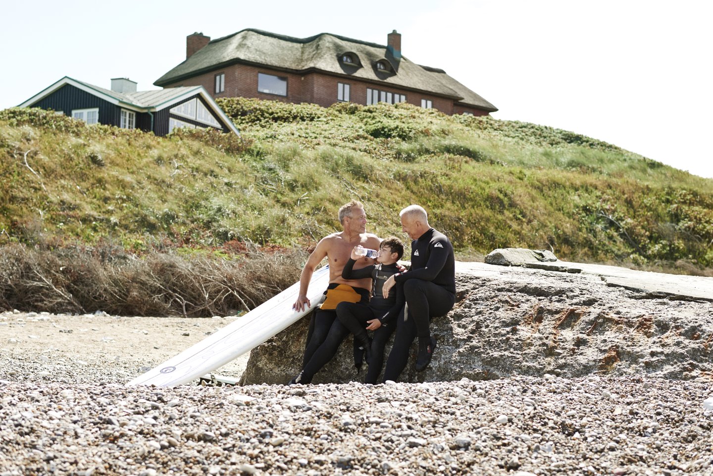 Two men and a child play on a beach beside a summerhouse in Denmark
