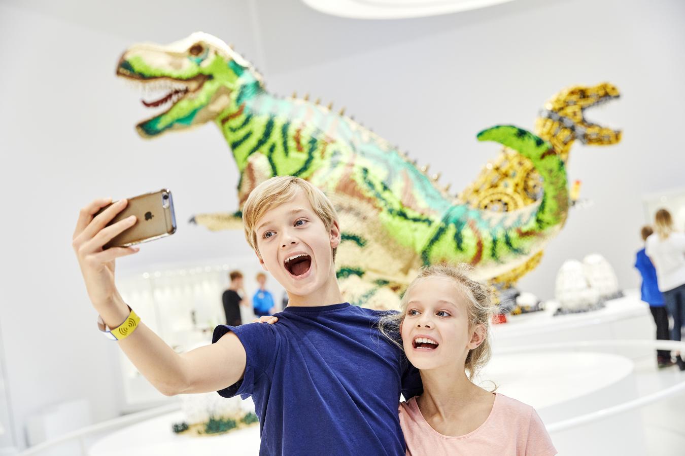 Geschwister machen ein Selfie vor den LEGO Dinosauriern im LEGO House in Billund