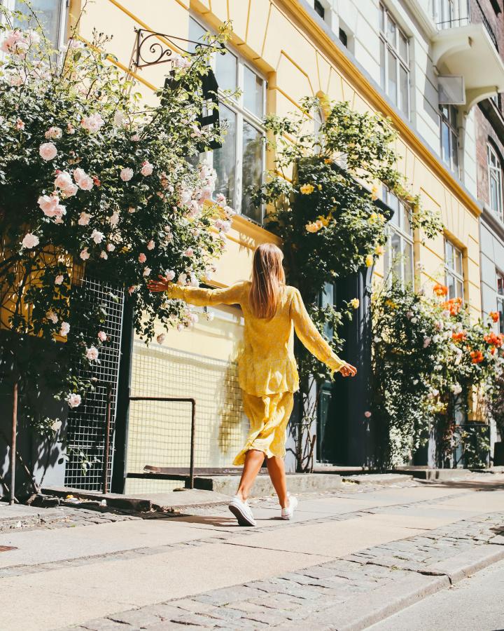 A girl in a yellow dress walks down a rose-lined Copenhagen street