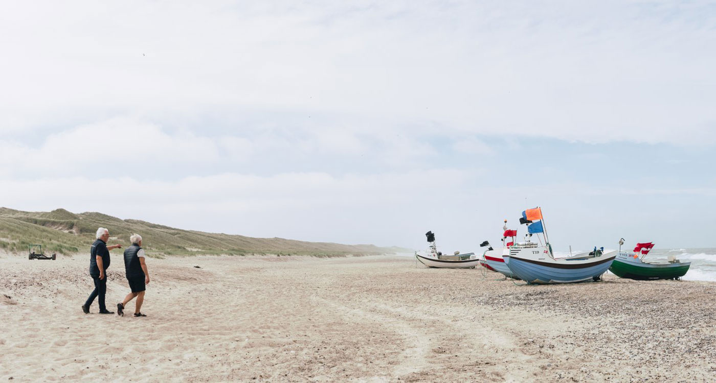 Two people take a walk beside boats on the beach at Snedsted, Thy National Park