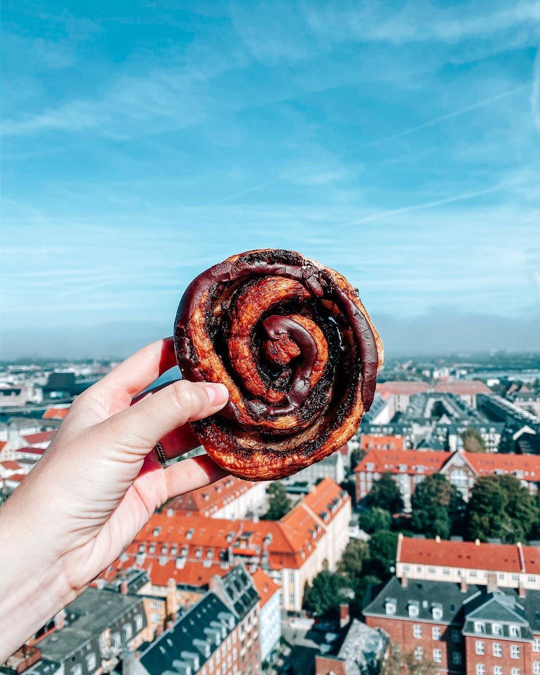 A danish pastry held out in front of the city streets