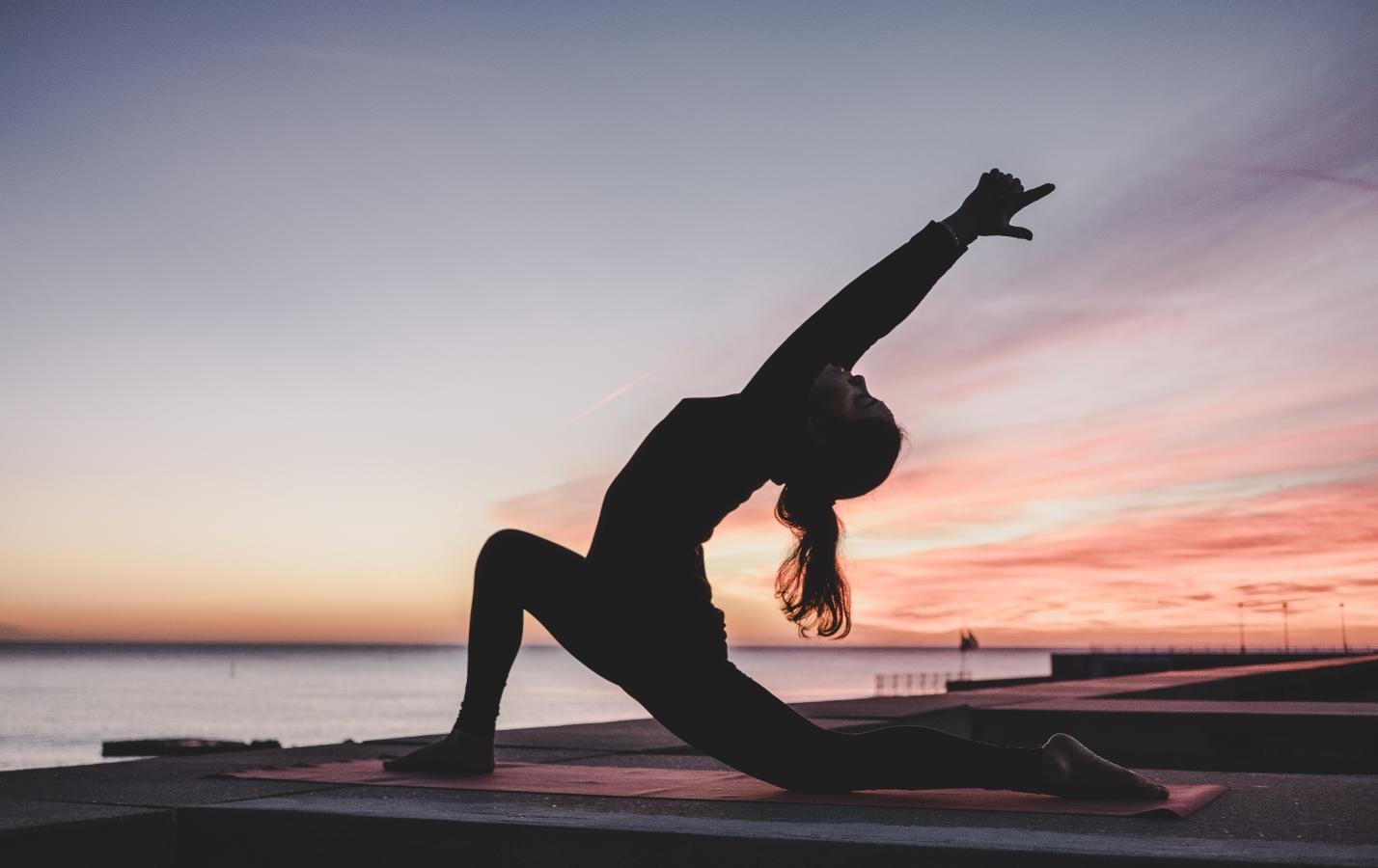 A lady does yoga on a SUP paddleboard by the sea as the sun sets