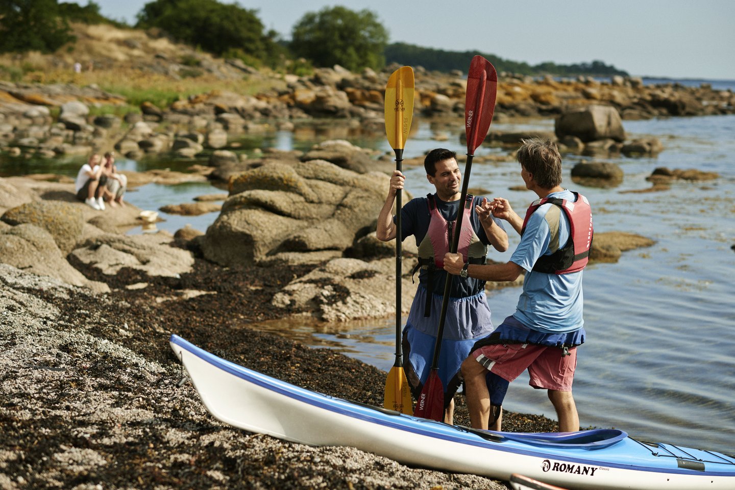 Two men standing by kayaks on the beach at Bornholm, Denmark