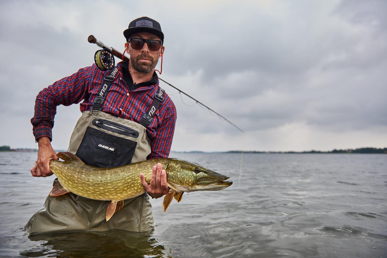 Mann steht im Wasser und hät einen großen Fisch in die Kamera, Dänemark