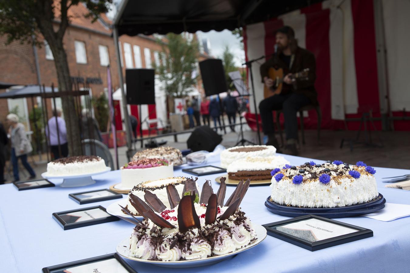 Bild von einem Tisch mit Kuchen und im Hintergrund einer Szene, Kuchenfestival in Sønderjylland 2021