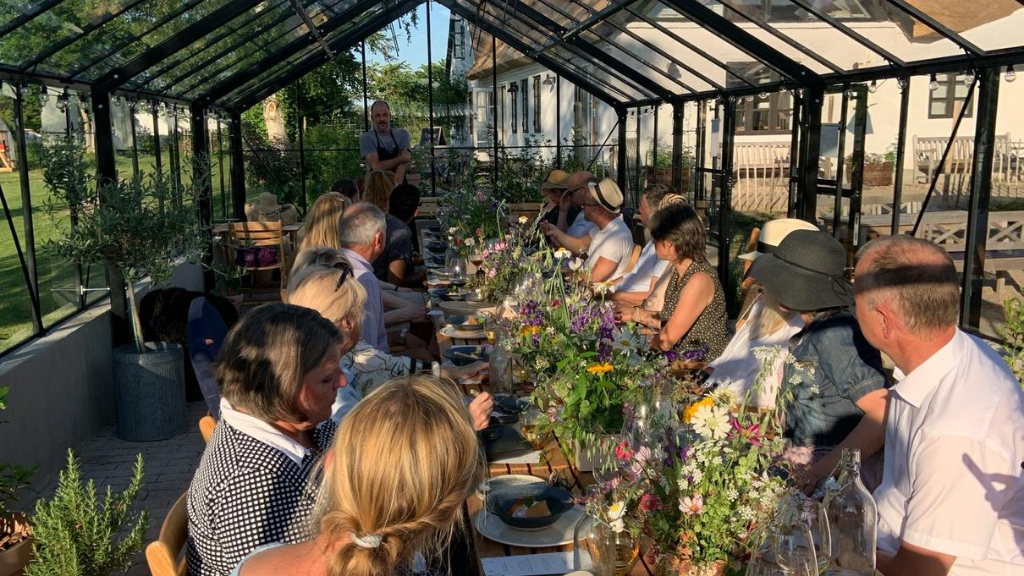 En gruppe mennesker nyter et måltid i drivhuset ved Rabarbergaarden, Nordsjælland
