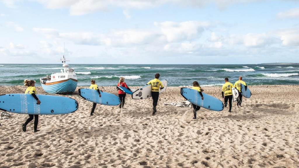 Surfere løper på stranden mot havet med surfebrett i armene ved Klitmøller, Danmark