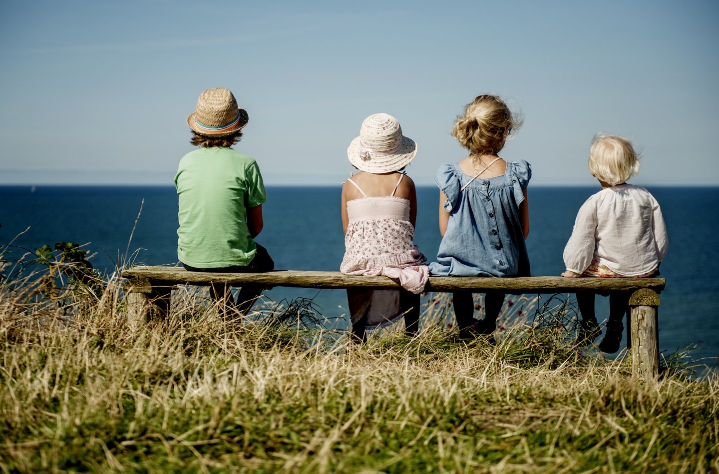 Four children sitting on a bench in Hanstholm, North Jutland, looking at the ocean.