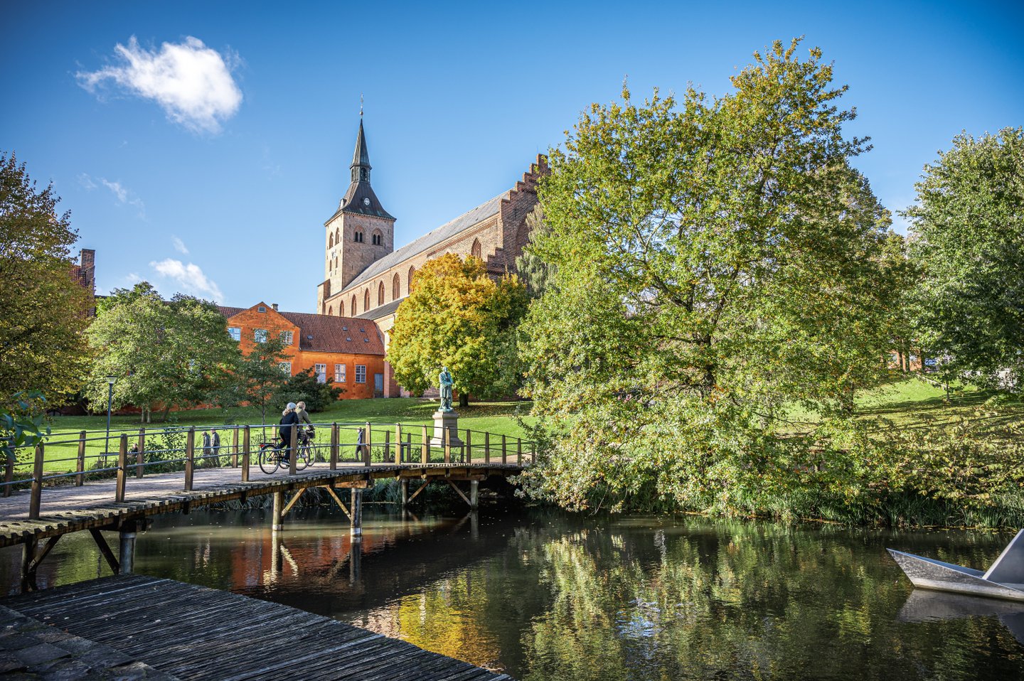 Fietsers rijden over de brug naar de sprookjestuin in Odense met de Odense Domkirke als achtergrond
