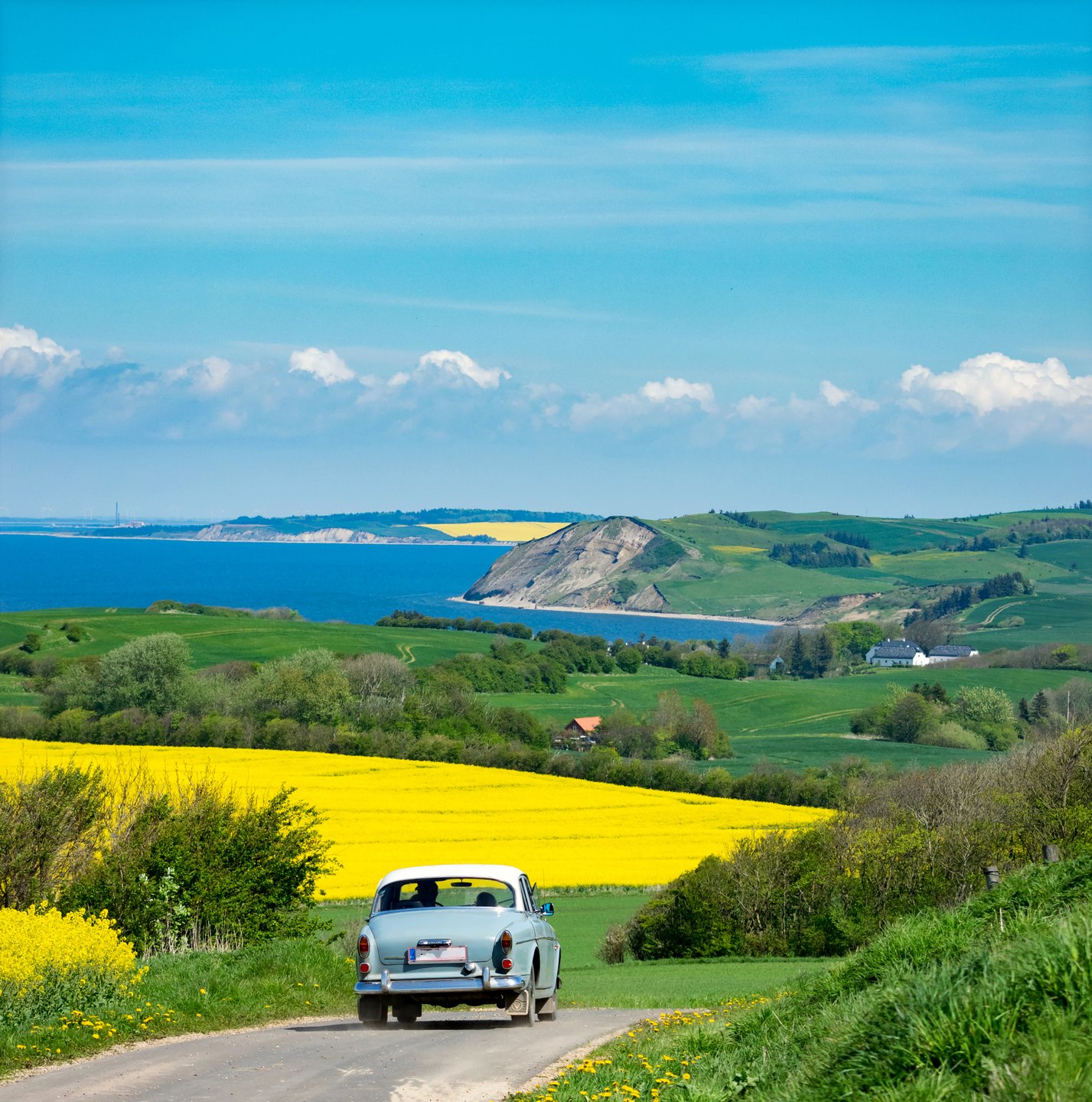 An old car driving through the hilly landscape on Mors Island in early summer.