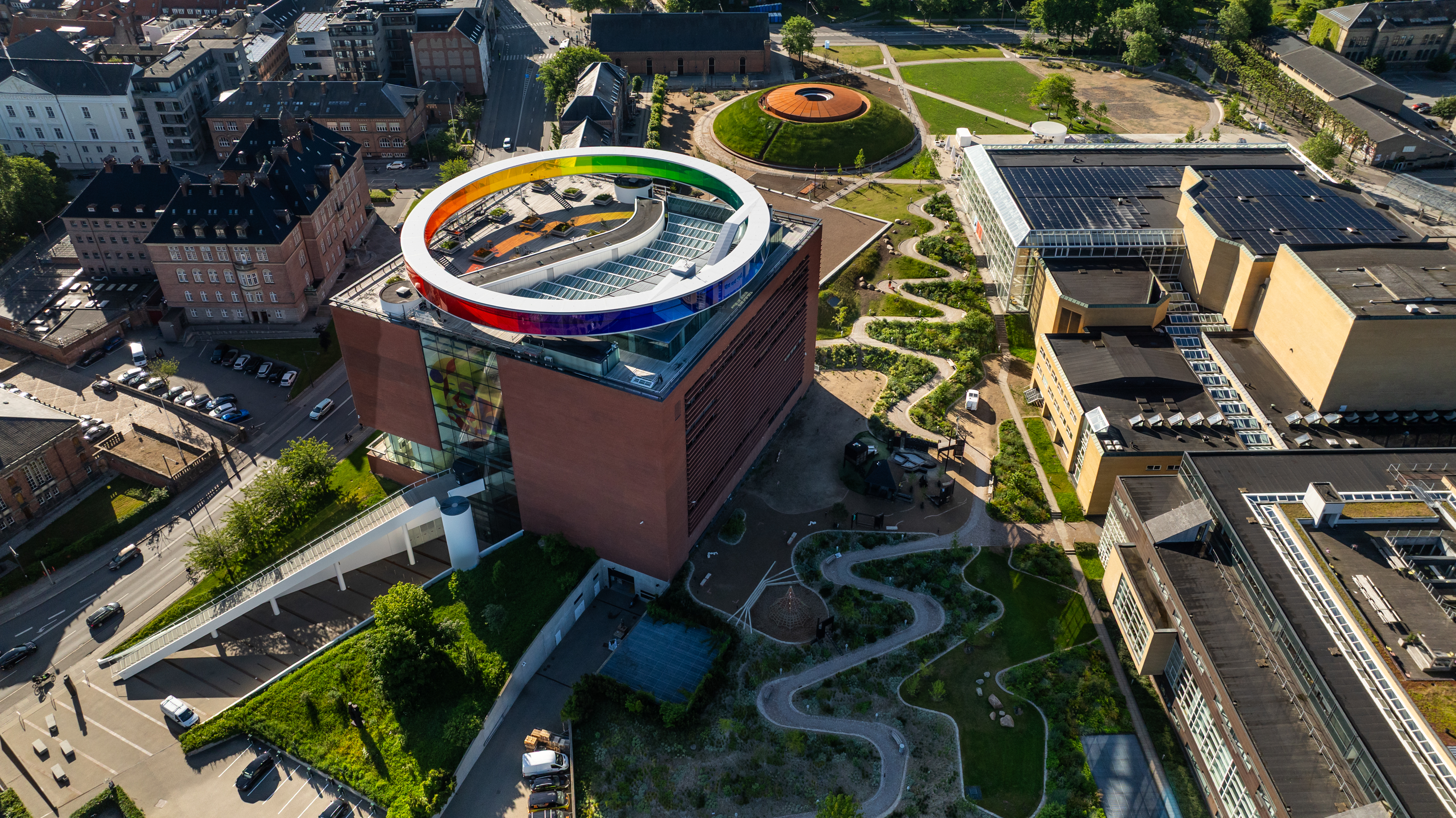ARoS Aarhus mit seinem ikonischen, regenbogenfarbenen Dachrundgang, umgeben von modernen Gebäuden und Grünflächen im Stadtzentrum.