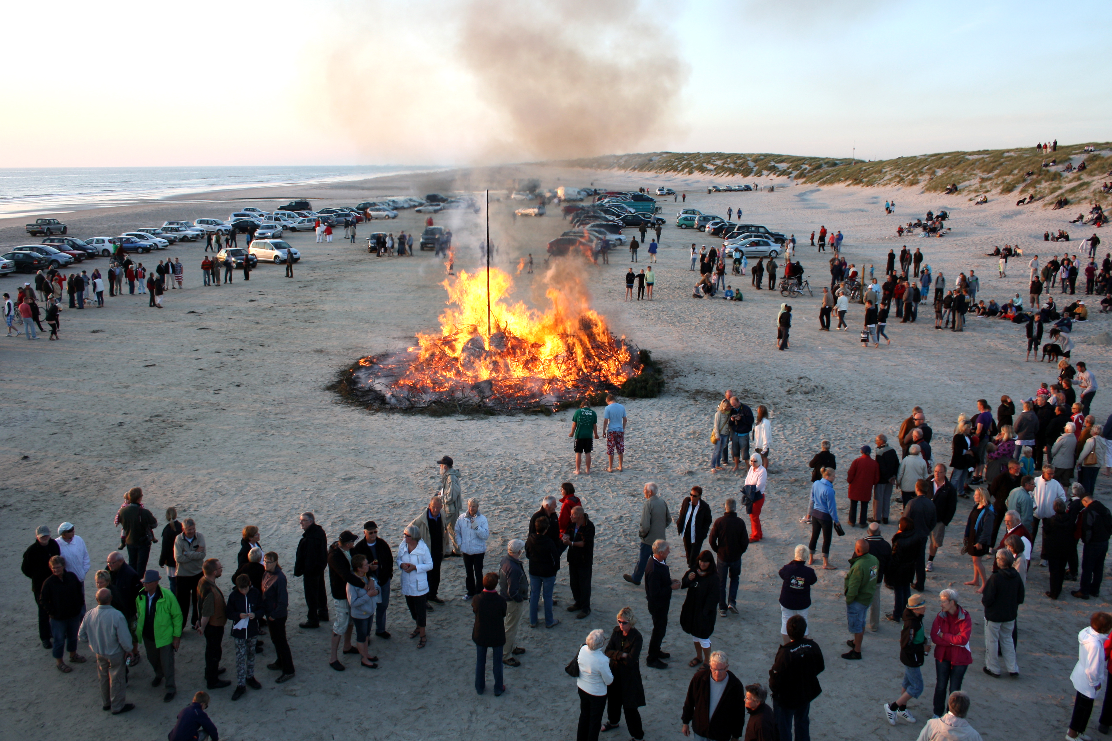 Menschen versammeln sich um ein großes Lagerfeuer am Strand während eines traditionellen dänischen Mittsommerfestes.