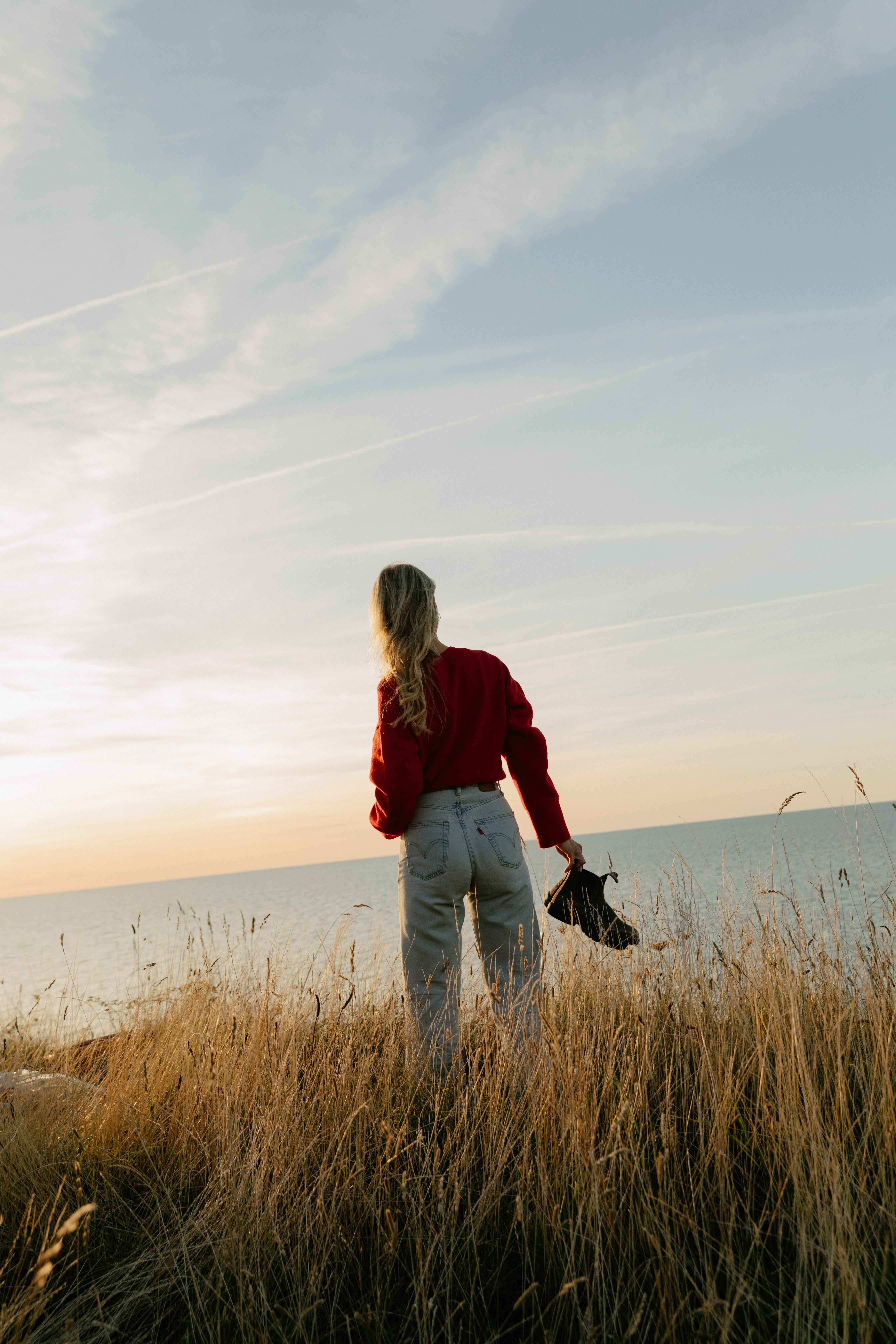 Frau schaut auf die Ostsee mit den Schuhen in der Hand