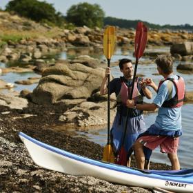 Two men standing by kayaks on the beach at Bornholm, Denmark
